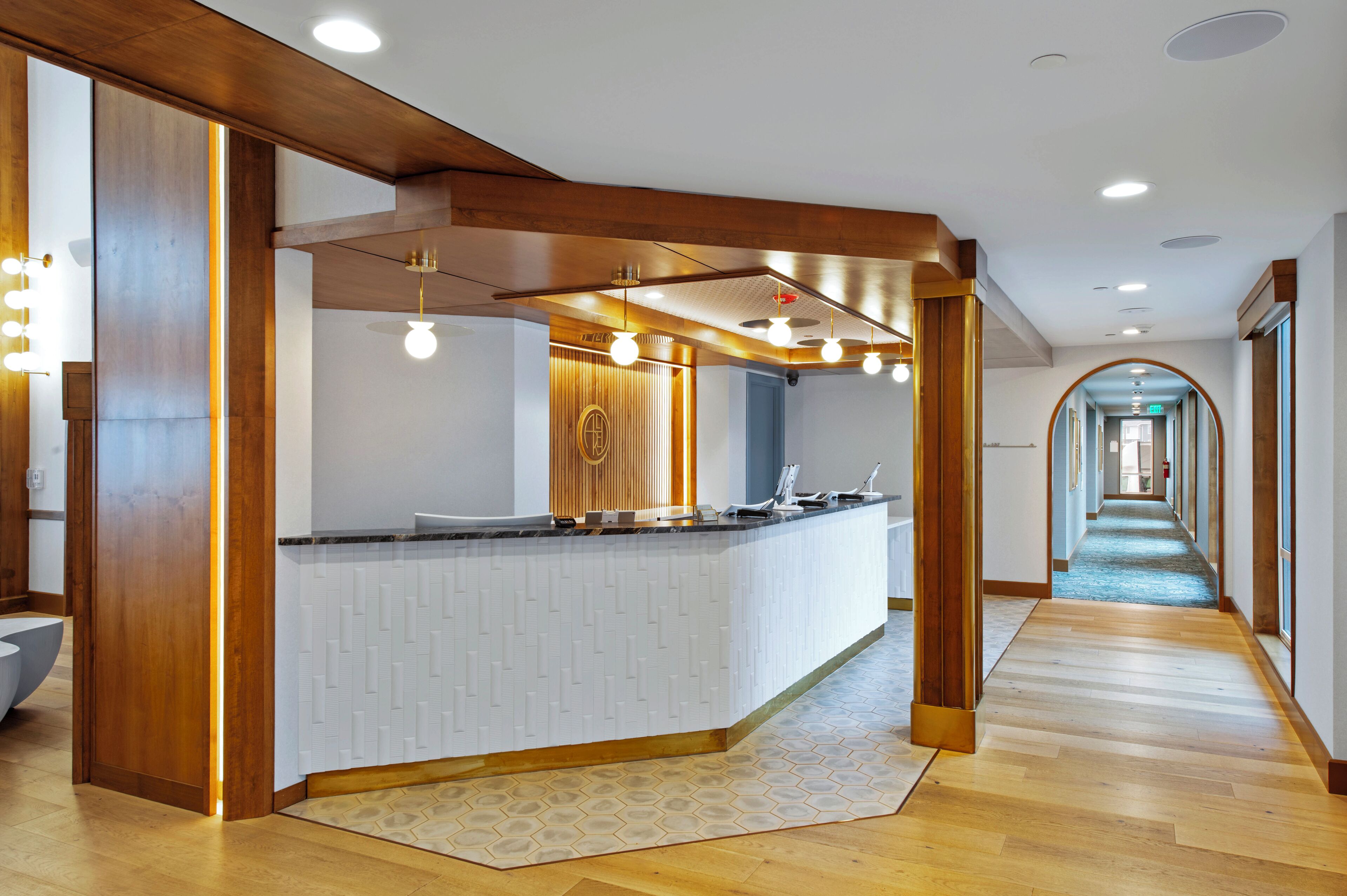 A modern reception area with a wooden reception desk, a patterned floor, and a hallway leading to other rooms.