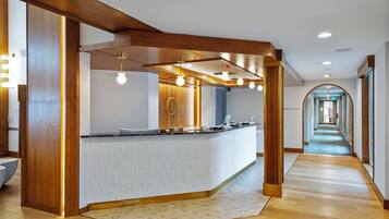 A modern reception area with a wooden reception desk, a patterned floor, and a hallway leading to other rooms.