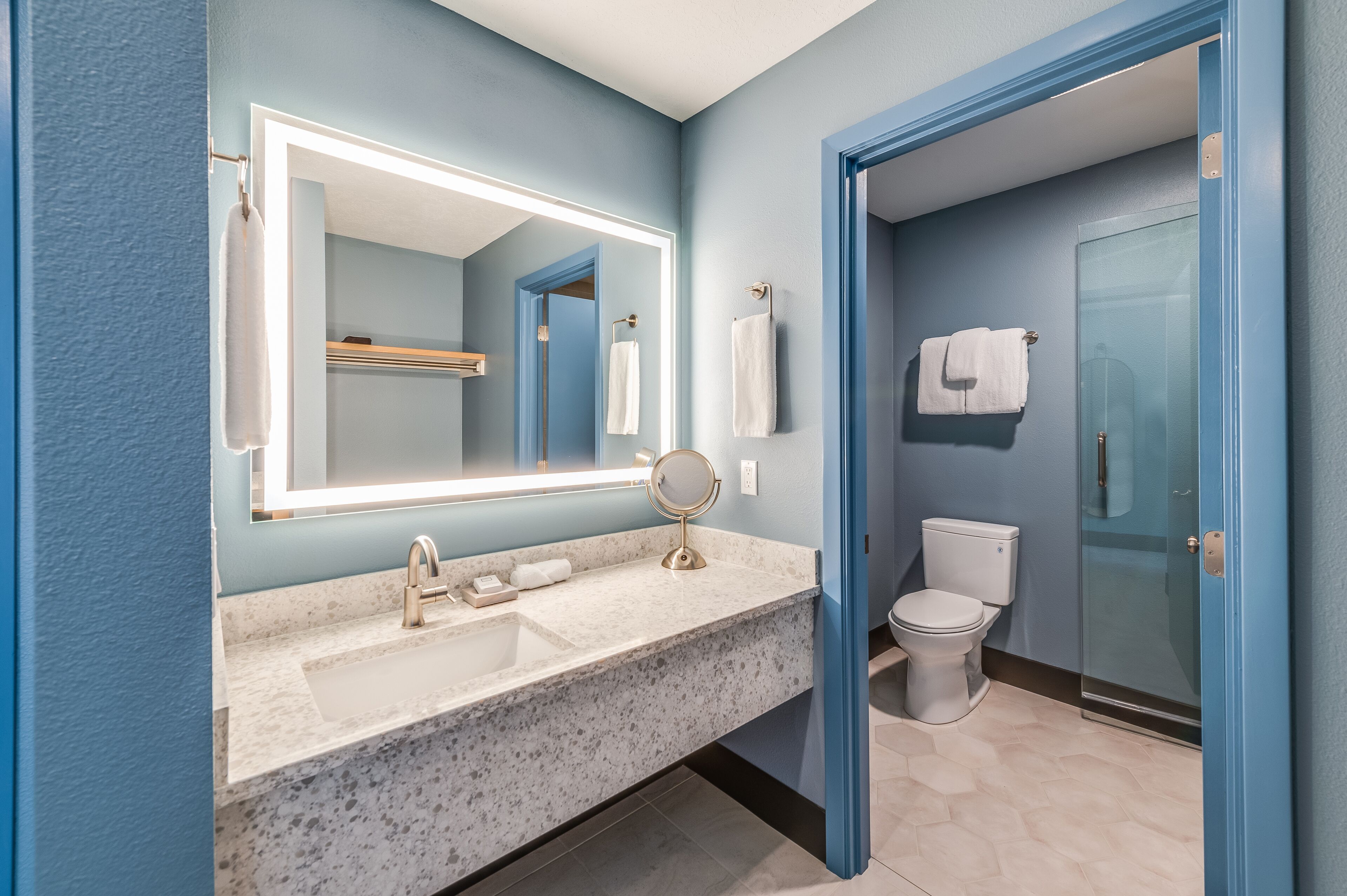 A bathroom with a marble sink, a large mirror, a toilet, and a glass shower door.