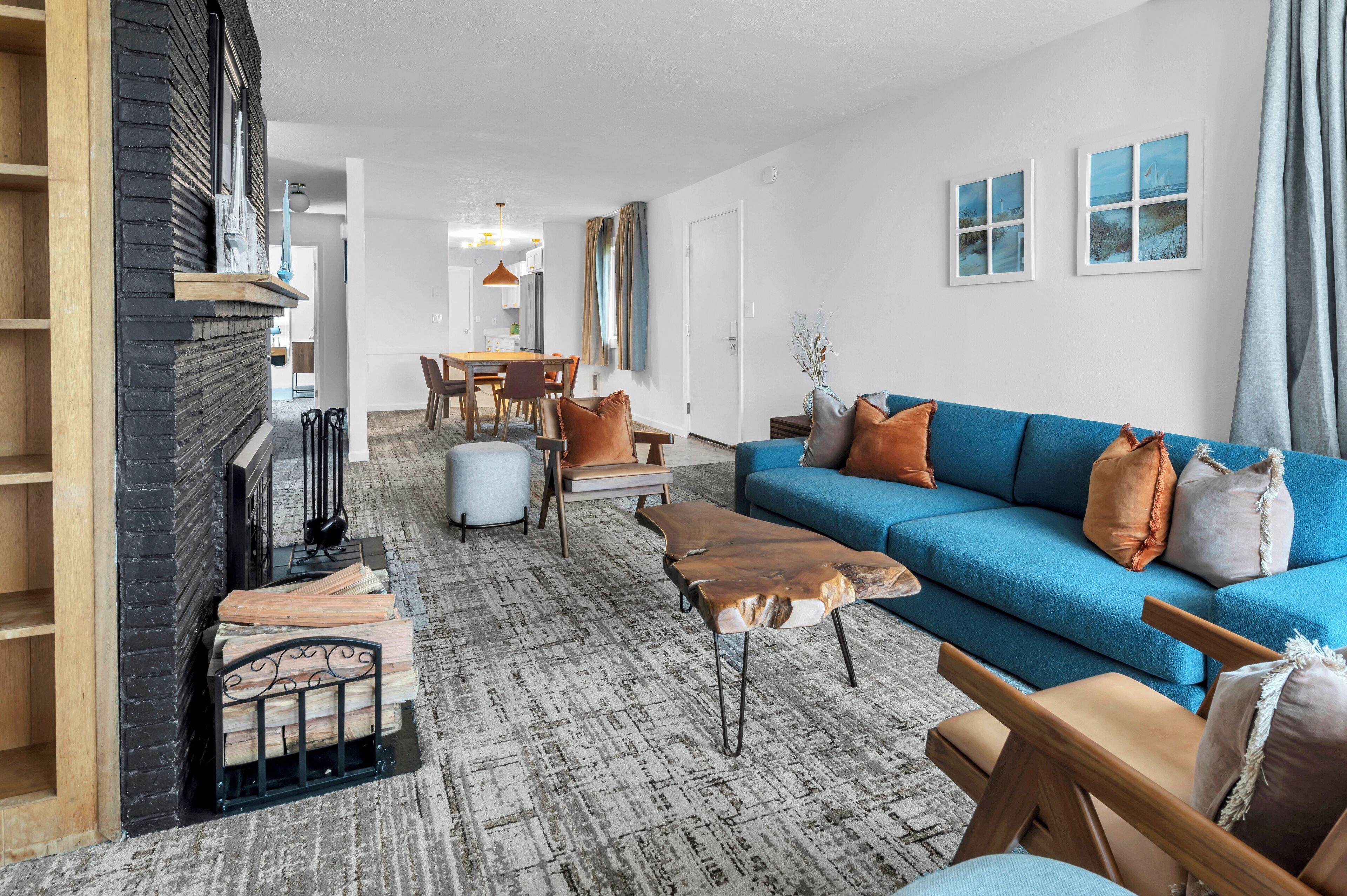 A modern living room with a blue sofa, leather coffee table, and a fireplace. There is a dining area in the background with a table and chairs.