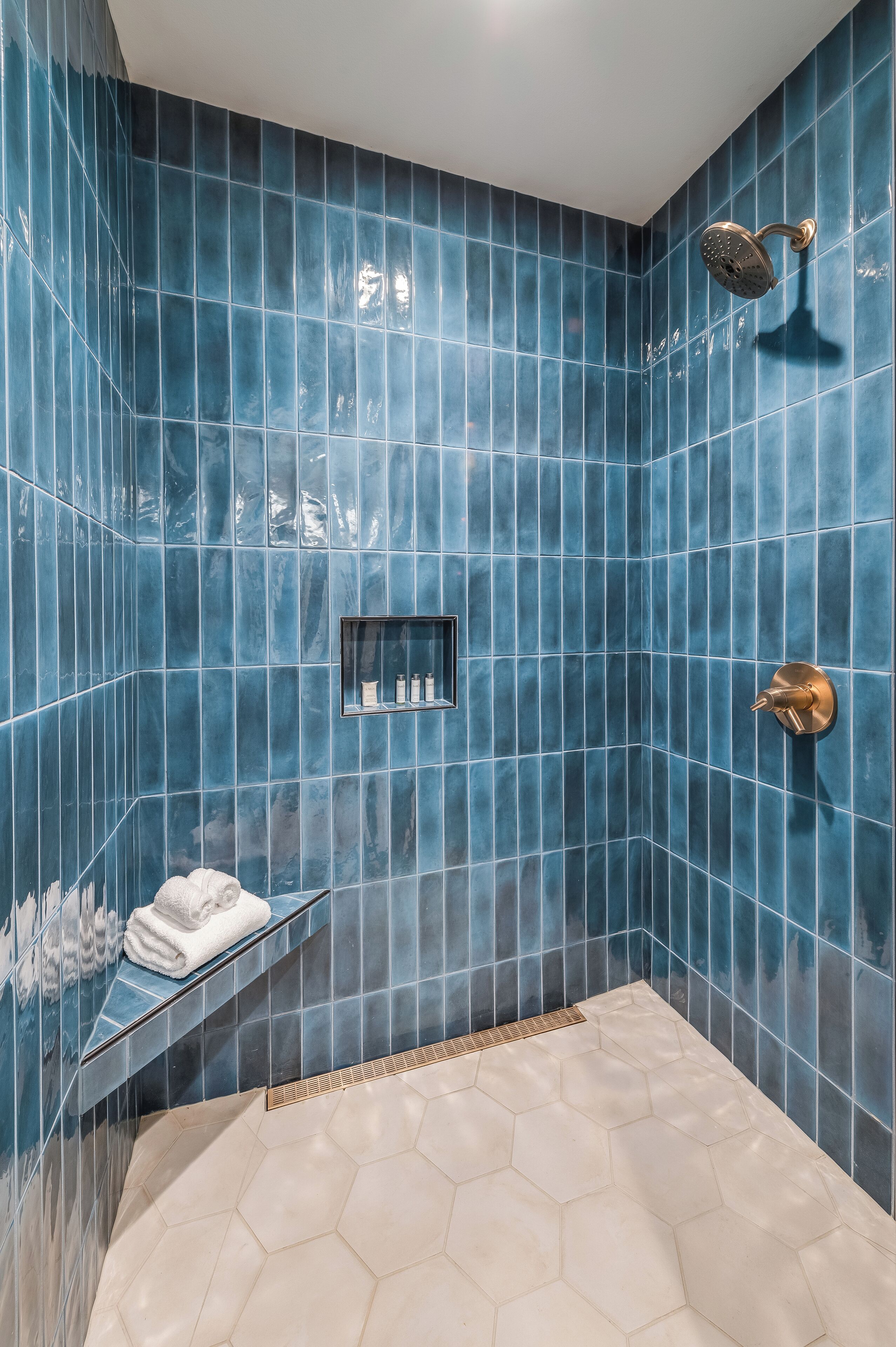 Ein Badezimmer mit blauen Fliesenwänden, einem sechseckigen Fliesenspiegel und einer Duschbrause sowie einem Handtuchhalter.
