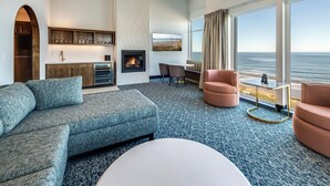 A modern living room with a fireplace, seating area, and a large window overlooking the ocean.