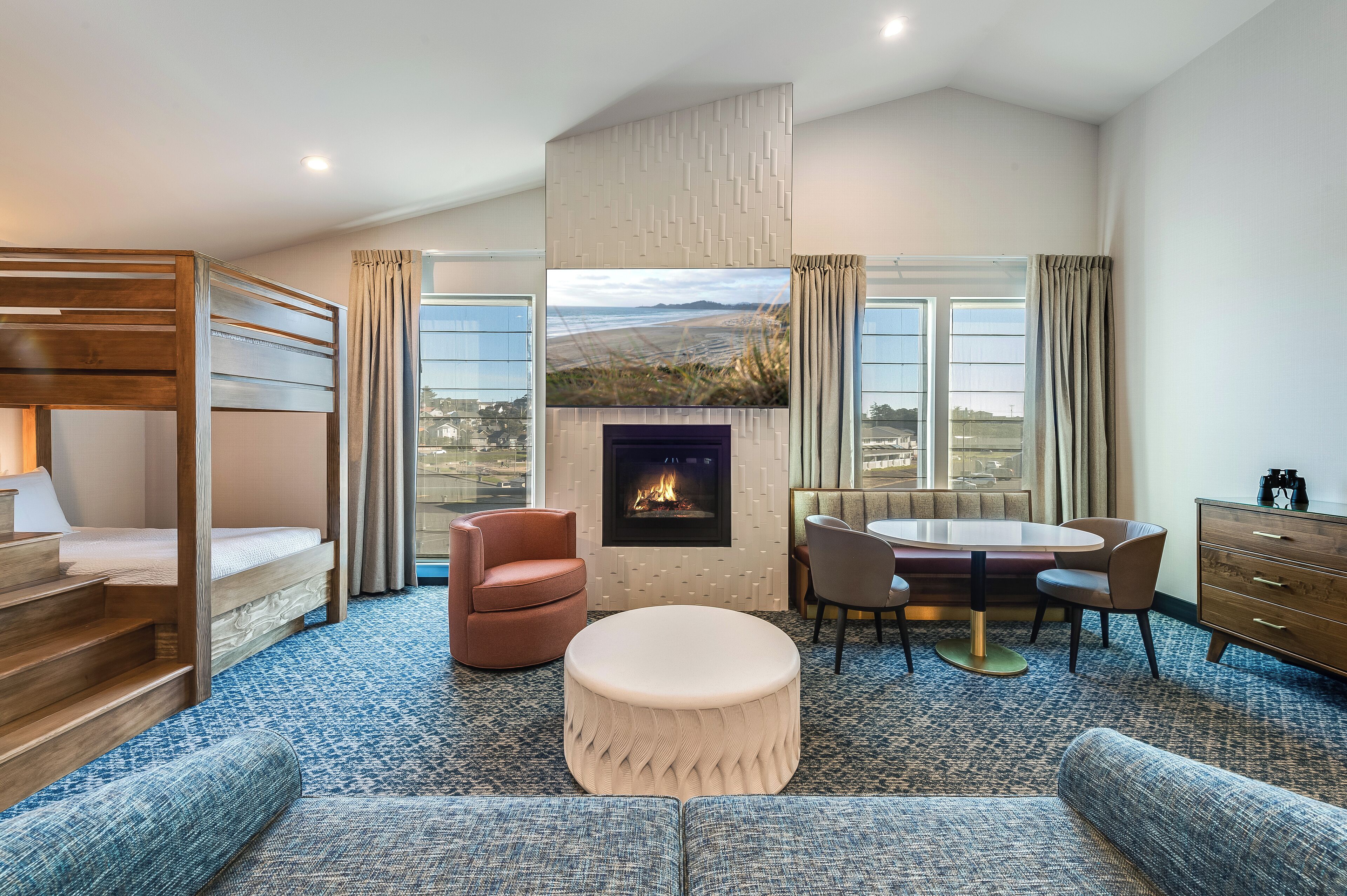 A modern hotel room with a bunk bed, a fireplace, a dining table with chairs, and a sofa.
