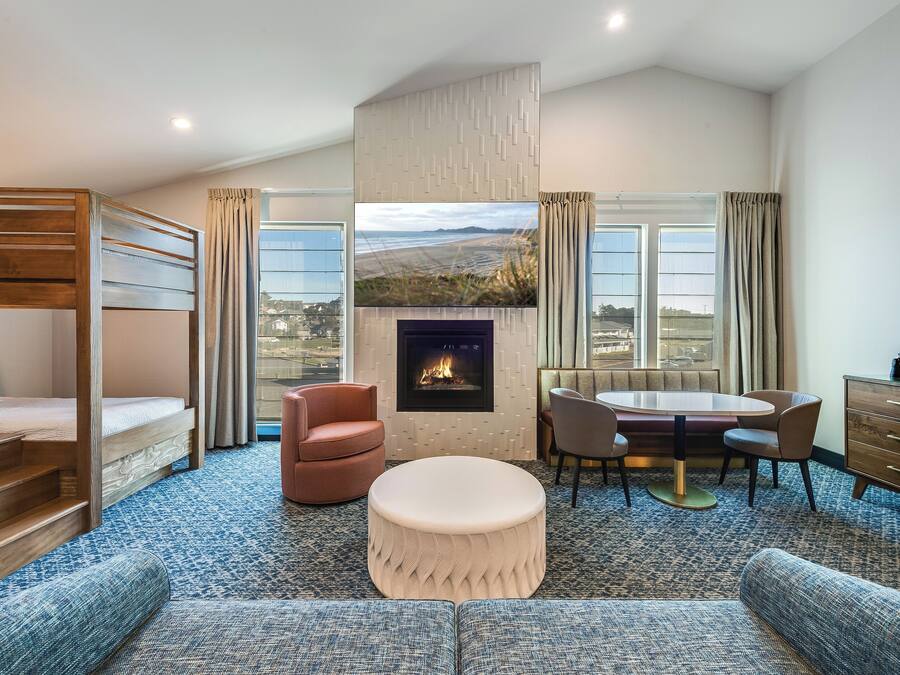 A modern hotel room with a bunk bed, a fireplace, a dining table with chairs, and a sofa.