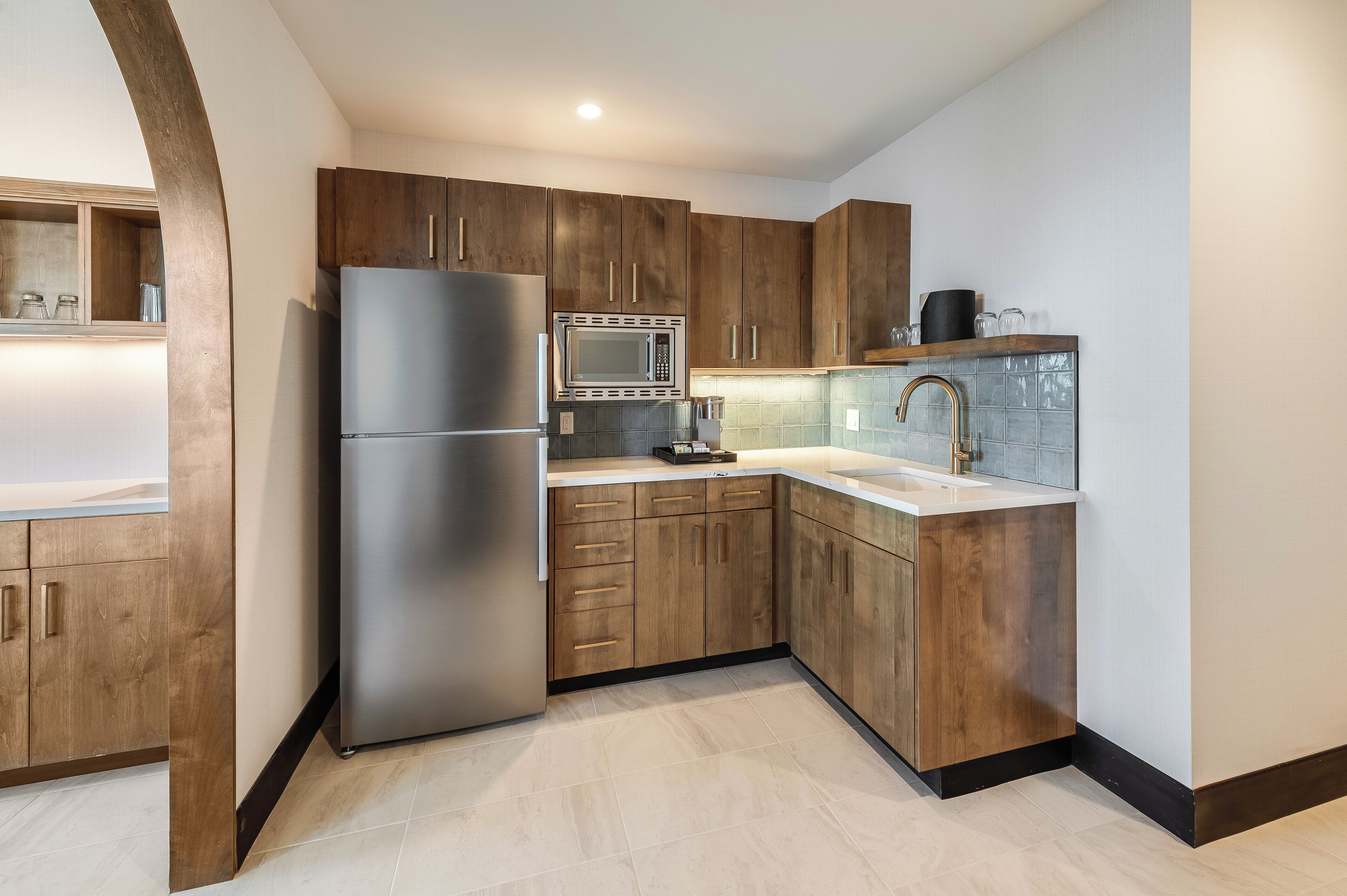 A modern kitchen with wooden cabinets, a stainless steel refrigerator, a microwave, and a sink.
