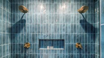 A bathroom with blue tiled walls, a rectangular shelf with toiletries, and two showerheads.