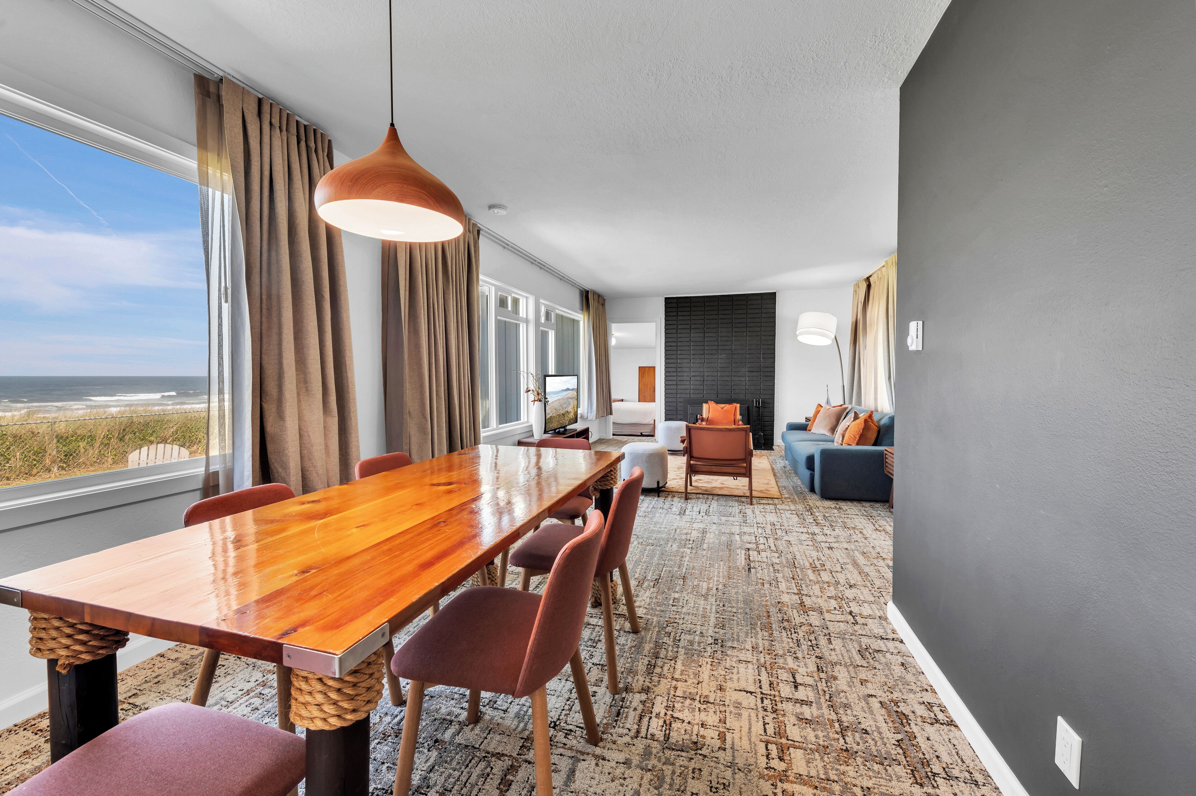 A modern living room with a large wooden dining table, comfortable seating, a sofa, and a view of the ocean.