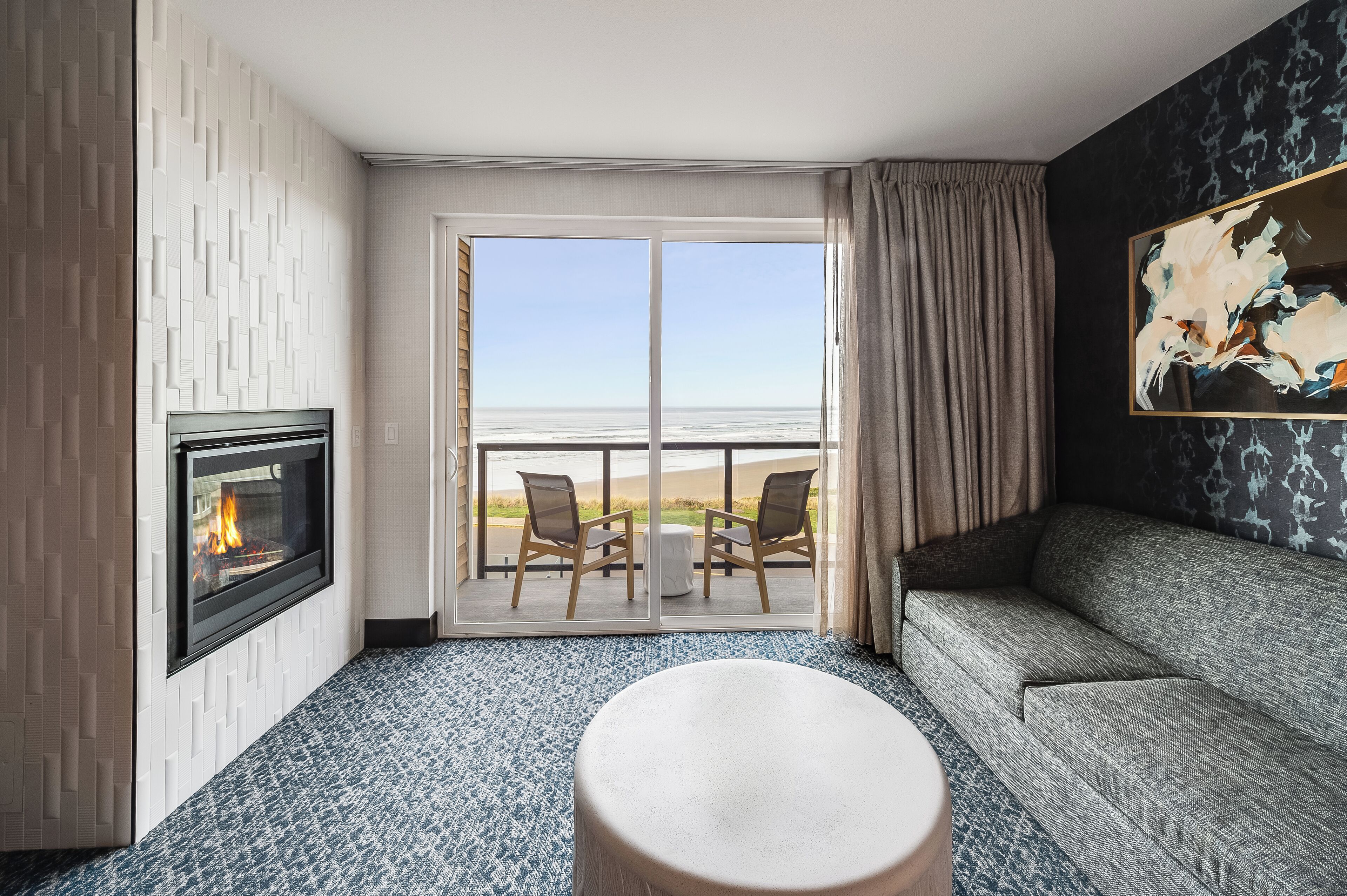 A hotel room with a fireplace, a sofa, a round table, and a balcony with chairs.