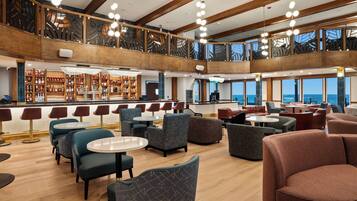 A spacious lounge area with multiple seating options, a bar with a variety of beverages, and a view of the sea.