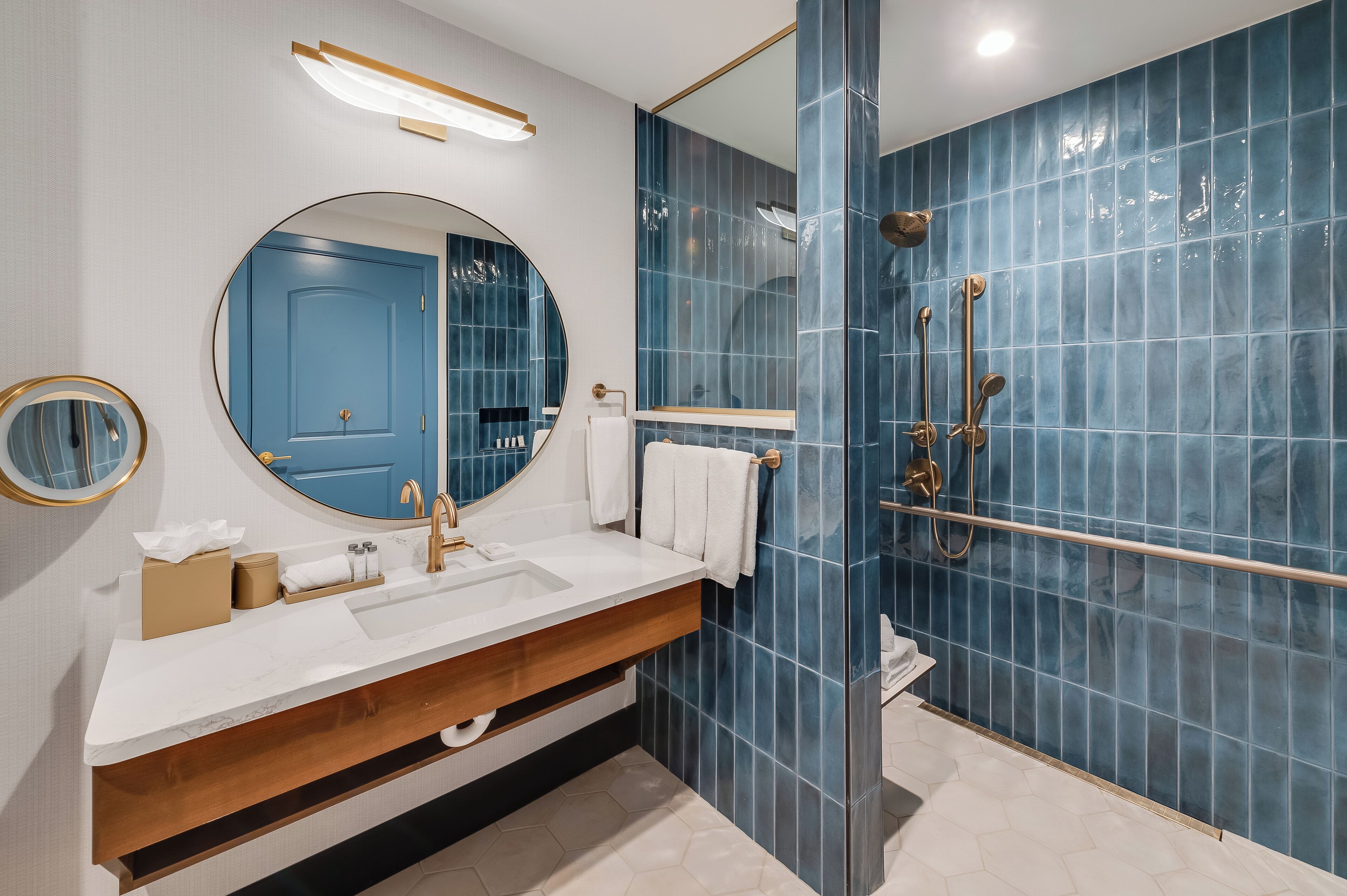 A modern bathroom with a large mirror, a white sink, and a shower with a glass door.