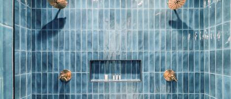 A bathroom with blue tiles, two showerheads, and a shelf with toiletries.