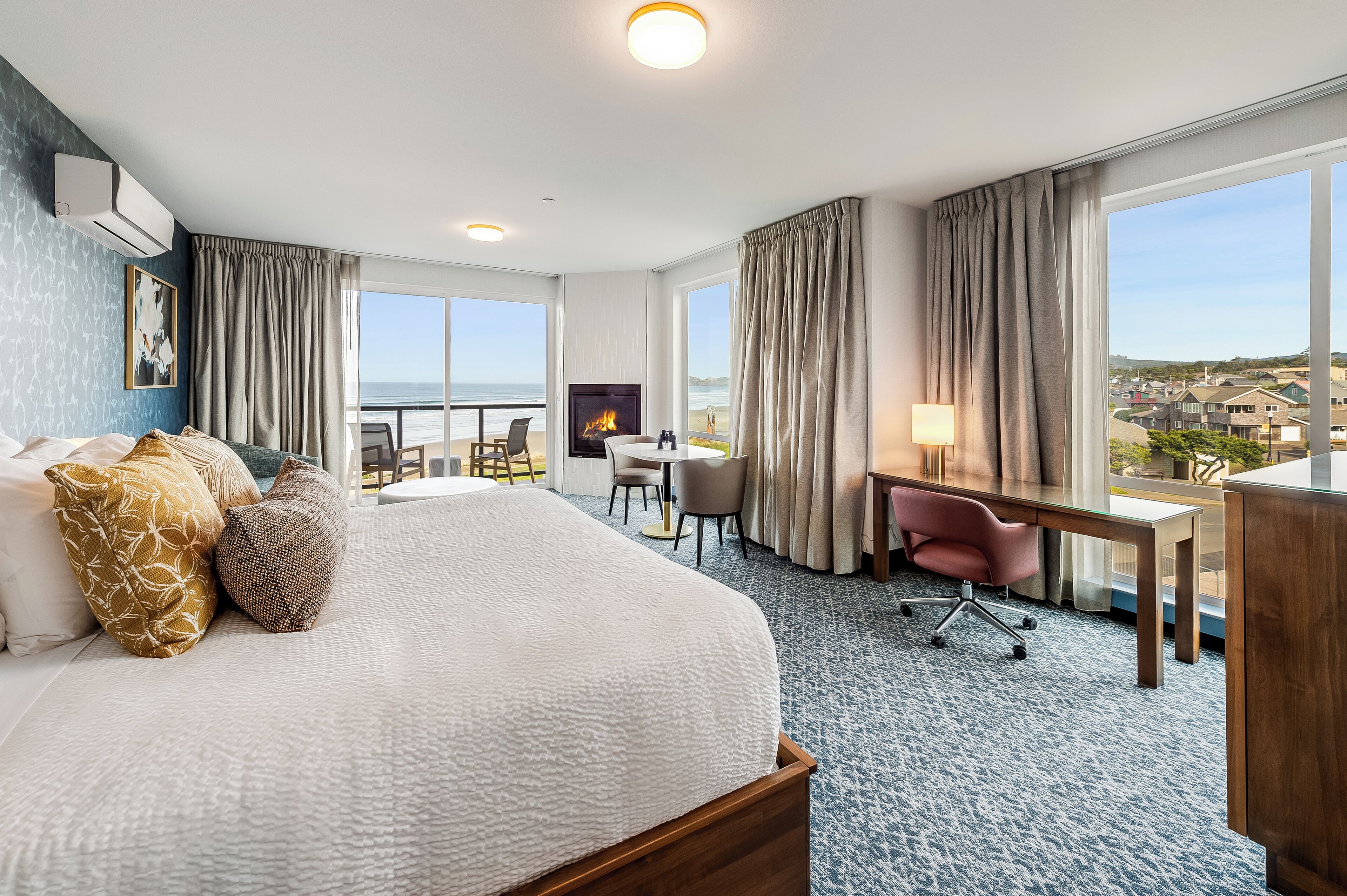 A hotel room with a large bed, a desk, a chair, and a view of the beach.