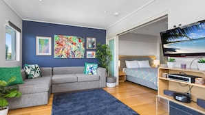 A modern hotel room with a grey sofa, a bed with patterned bedding, a flat-screen TV, and artwork on the walls. - Resort & Spa 6316 withTropical Pool Views - 230m to Beach (KINGSCLIFF)