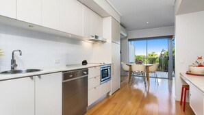 A modern kitchen with white cabinetry, stainless steel appliances, and a wooden floor. - Resort & Spa 6316 withTropical Pool Views - 230m to Beach (KINGSCLIFF)