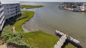 Una propiedad frente al agua con un terraplén cubierto de césped, un muelle de madera y un edificio moderno con varios balcones.