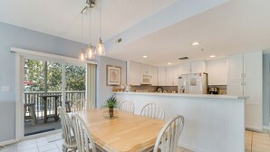 Una cocina amplia con armarios blancos, una mesa de comedor de madera y luces colgantes.