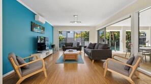 A modern living room with a TV, sofa, and chairs, large windows, and a view of the outdoors.