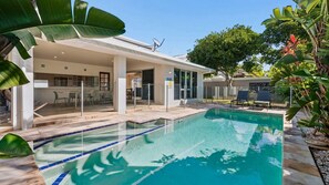 A swimming pool with a clear blue water, surrounded by a covered patio area with chairs and a table.