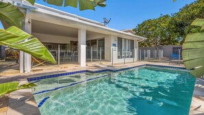 A modern pool area with clear water, a covered patio, and a glass door entrance.