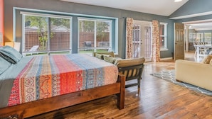 Un dormitorio con una cama grande, suelo de madera y vistas al patio trasero por una ventana.