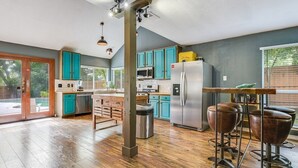 Una cocina amplia con armarios azul verdosos, un refrigerador de acero inoxidable y una mesa de madera con taburetes.
