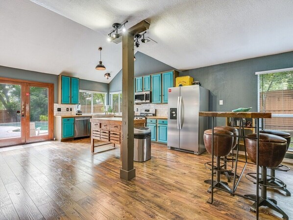 Une cuisine spacieuse avec des meubles de couleur turquoise, un réfrigérateur en acier inoxydable et une table à manger en bois, accompagnée de tabourets.