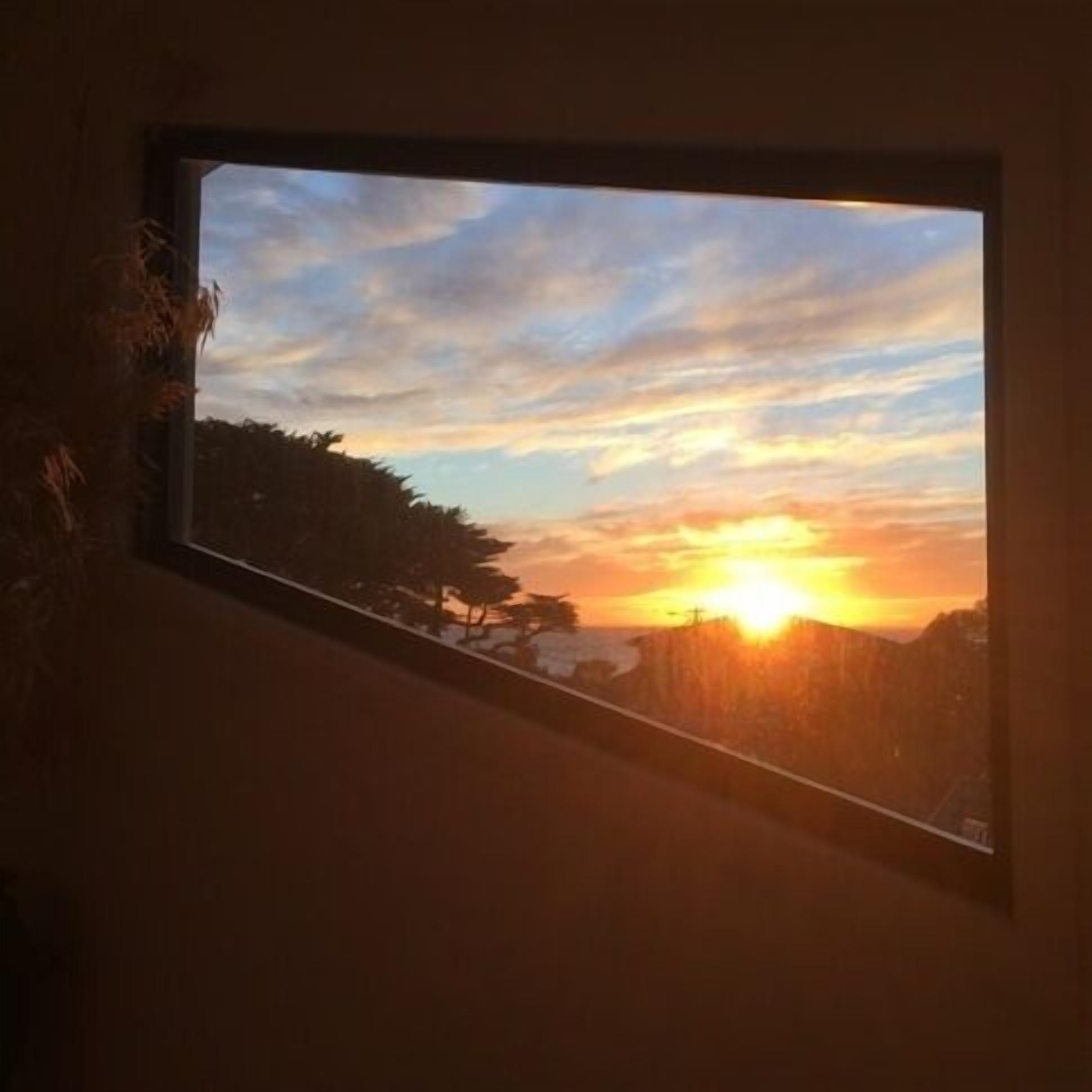 Una ventana con vistas a la puesta de sol sobre un paisaje montañoso.