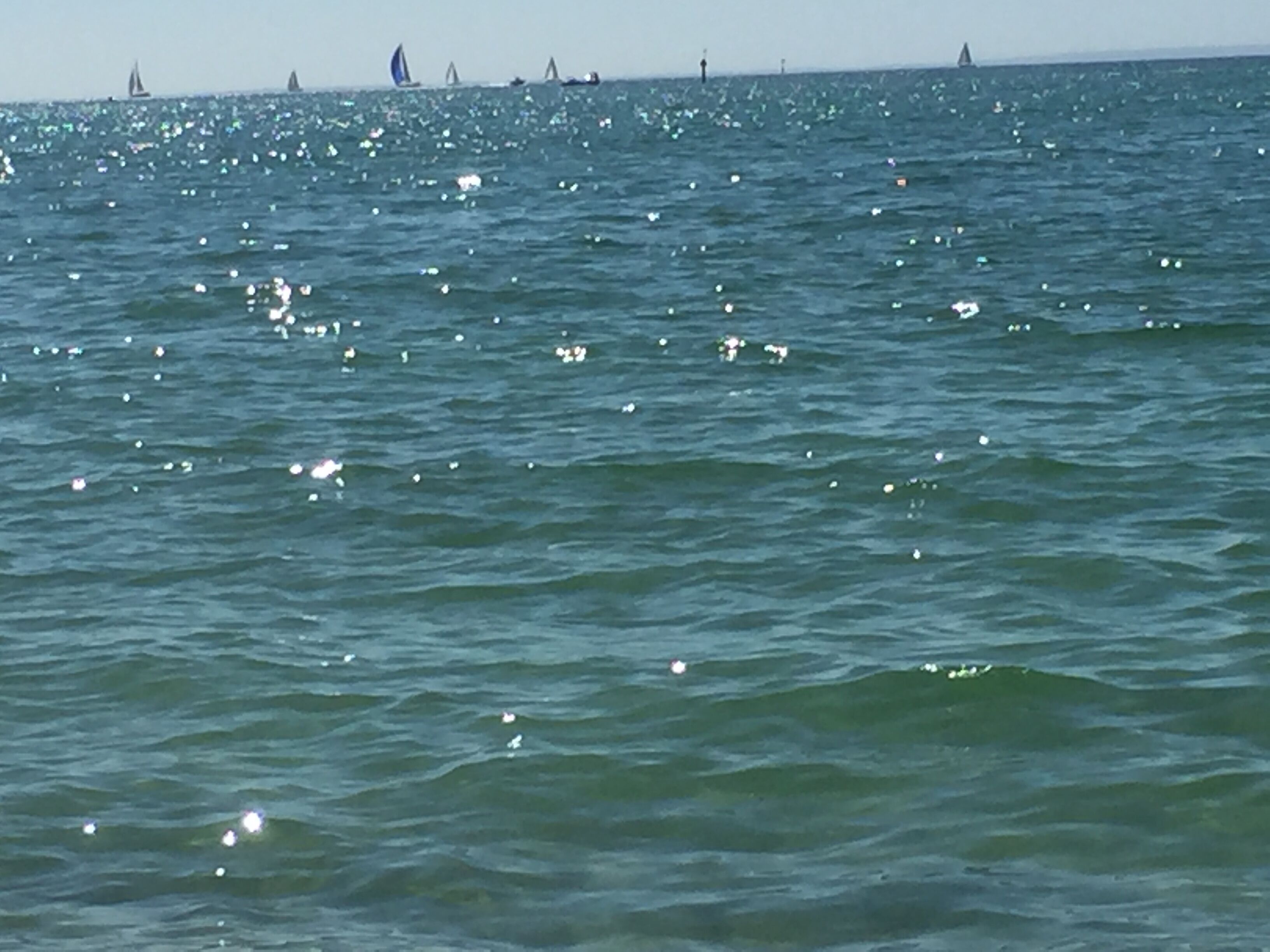 A body of water with several sailboats and a lighthouse in the distance.