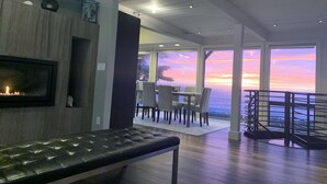 A modern interior with a fireplace, dining area, and large windows overlooking a scenic view. - Bodega Bay - Magical Ocean Front View- Doesn’t get better than this!! (Bodega Bay)