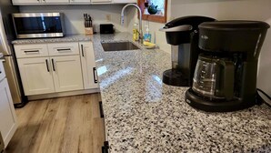 Eine Küche mit weißen Schränken, einer Arbeitsplatte aus Granit, einer Kaffeemaschine und einer Mikrowelle.