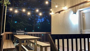 Eine Holzdiele mit Grill und Tisch, umgeben von Lichterketten.