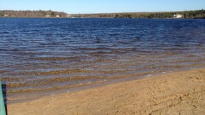 Ein Sandstrand mit klarem Wasser und einer entfernten Küstenlinie mit Gebäuden.