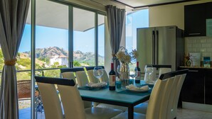 A dining area with a table set for two, a refrigerator, and a view of the hills. - Stunning Oceanview Villa, Private Jacuzzi, 3 bedrooms, minutes from downtown (Playas del Coco)
