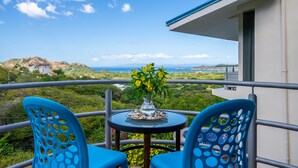 A balcony with two blue chairs, a small table with a vase of yellow flowers, and a view of a mountainous landscape. - Stunning Oceanview Villa, Private Jacuzzi, 3 bedrooms, minutes from downtown (Playas del Coco)