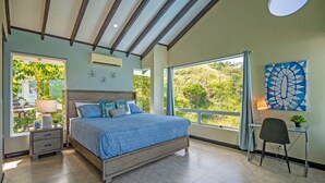 A bedroom with a large bed, a desk, and a view of greenery. - Stunning Oceanview Villa, Private Jacuzzi, 3 bedrooms, minutes from downtown (Playas del Coco)
