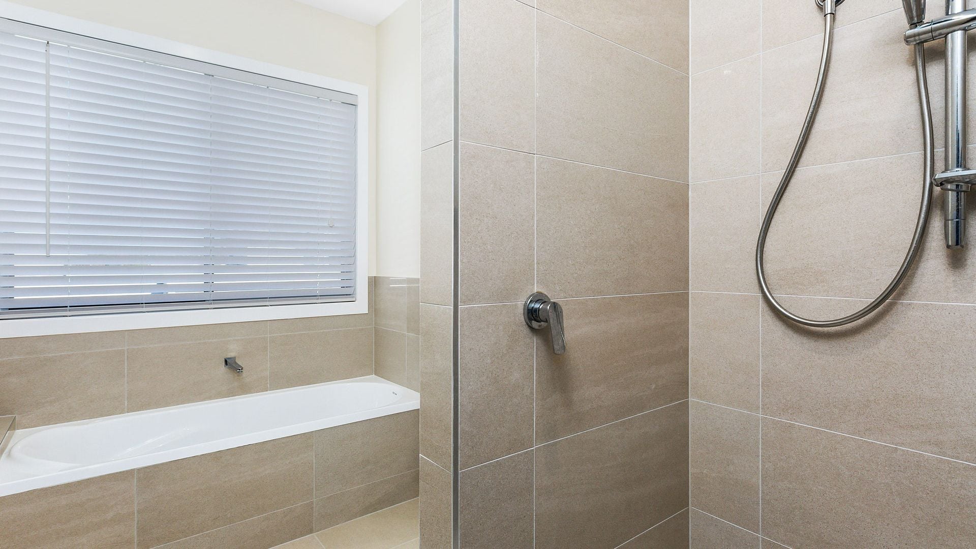 A bathroom with a bathtub, a shower, and a window with blinds.