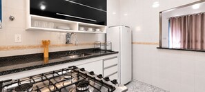 Une cuisine équipée d’une cuisinière à gaz, de meubles blancs, d’un réfrigérateur et d’une fenêtre avec des rideaux.