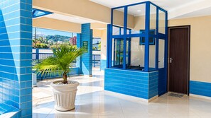 Eine Hotelhalle mit blau gefliestem Boden, einer Kübelpalme und einem gläsernen Sitzbereich.