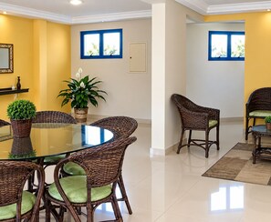 Un comedor con mobiliario de mimbre y una mesa de vidrio, paredes amarillas y ventanas con marcos azules.