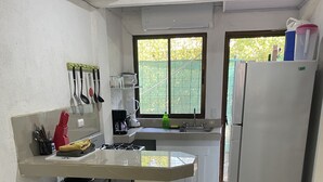 A compact kitchen with a white countertop, a sink, a stove, and a refrigerator. There is a window with a view of greenery outside. - Rita & Sonny Beach Apt-B (Tamarindo-Playa Callejones)