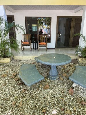 Un espacio al aire libre con una mesa redonda y bancos, rodeado de piedras y plantas en macetas.