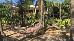 A house with a porch, surrounded by palm trees and hammocks. - Rita & Sonny Beach Apt-B (Tamarindo-Playa Callejones)