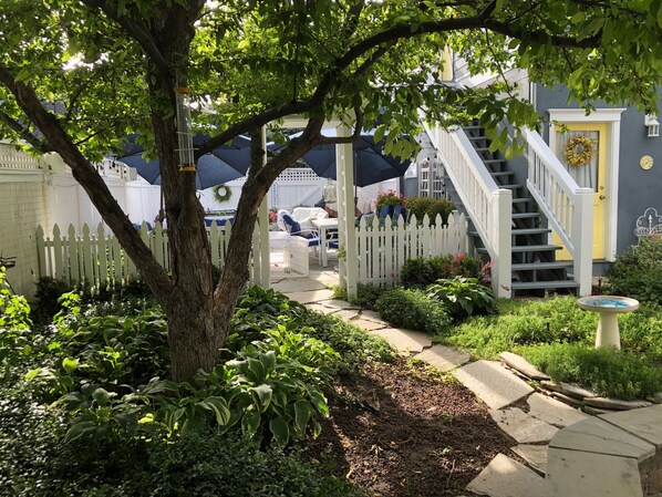 A garden pathway leading to a house with a white picket fence, a staircase, and a yellow door. - Charming Carriage House In Prospect New Town (Longmont)