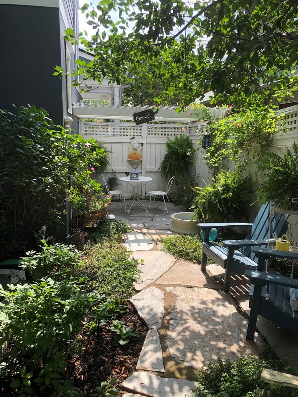 A garden patio with a white table and chairs, surrounded by lush greenery and a decorative fountain. - Charming Carriage House In Prospect New Town (Longmont)