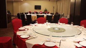 Un salón de conferencias con mesas redondas, sillas rojas y manteles blancos.