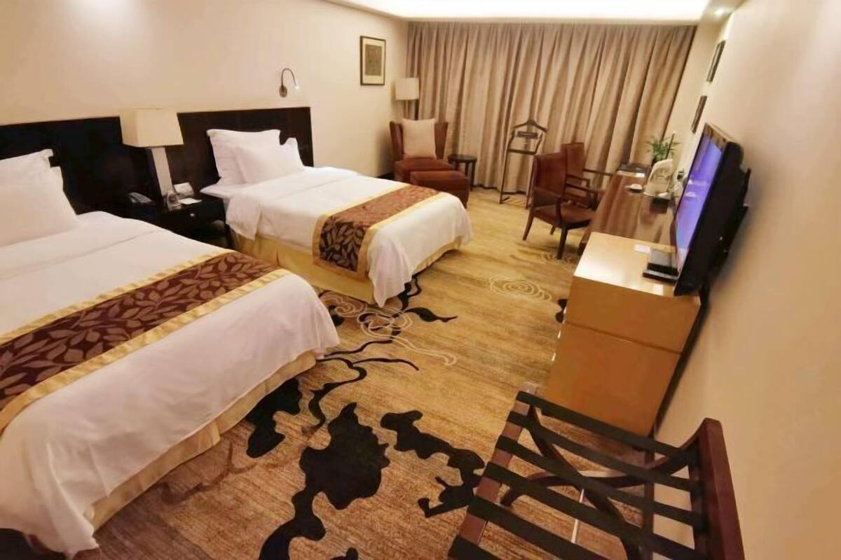 A hotel room with two beds, a desk, a chair, a television, and a carpet with a cow print design.