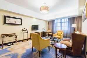 Hotelkamer met een bank, fauteuils, een salontafel, een televisie, een bureau en een lamp.