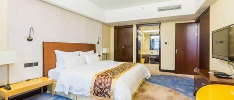 A hotel room with a bed, bedside table, lamp, chair, television, and a carpeted floor.