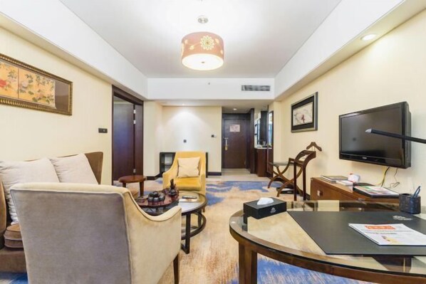 Een hotelkamer met een bank, fauteuils, een kleine tafel, een televisie en een vloerbedekking.
