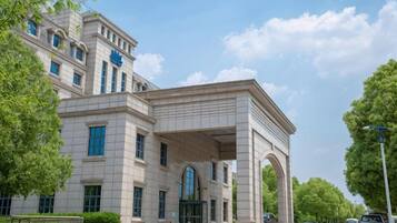 A large, classical building with a prominent archway entrance, multiple windows, and a paved driveway.
